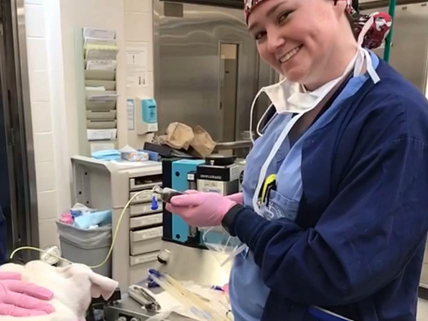 Tamar Minick in surgical gown and cap smiling while preparing anesthetic equipment in surgery