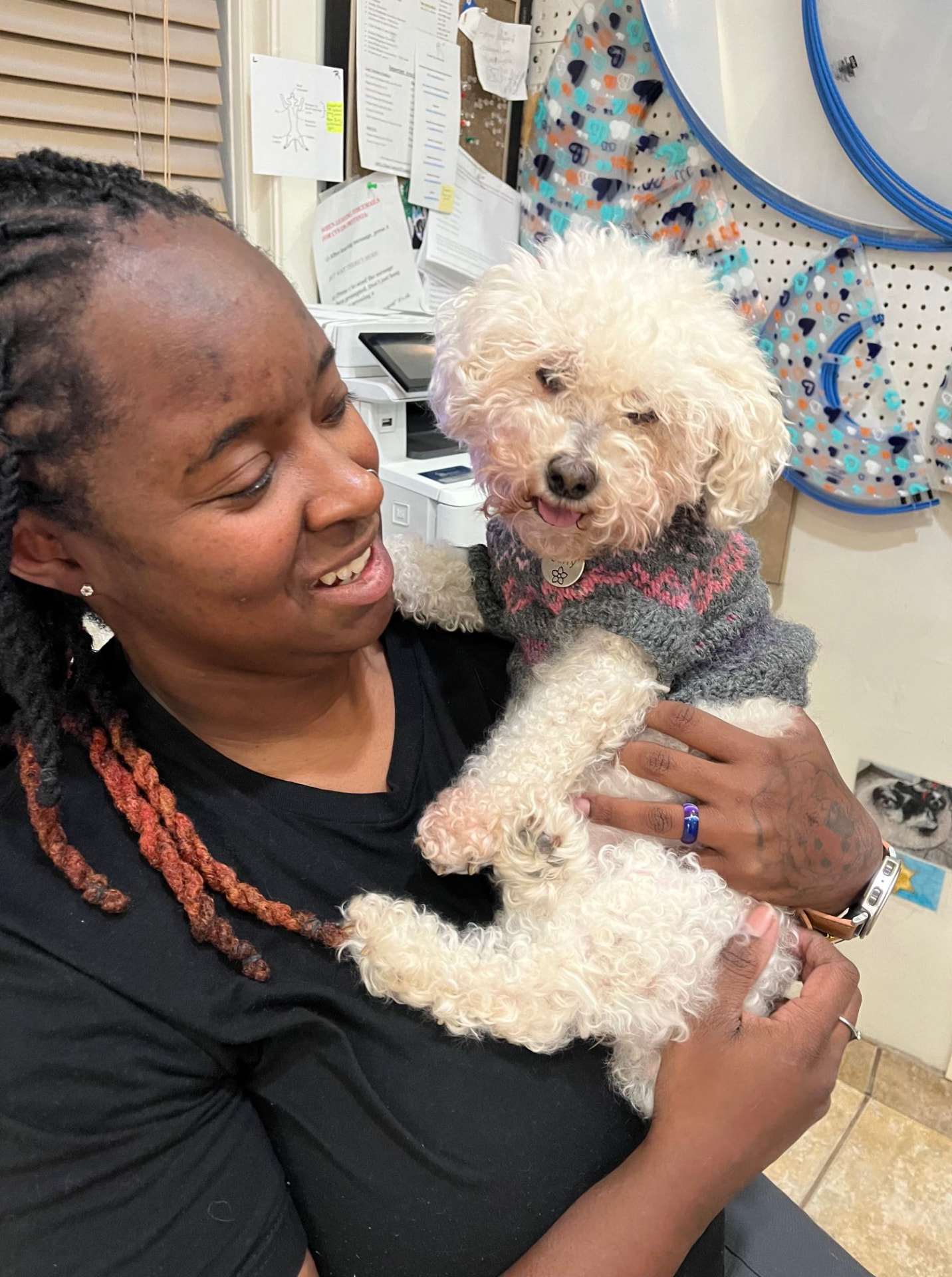 Alicia Lee Jones smiling at a white poodle in a knit sweater she is holding