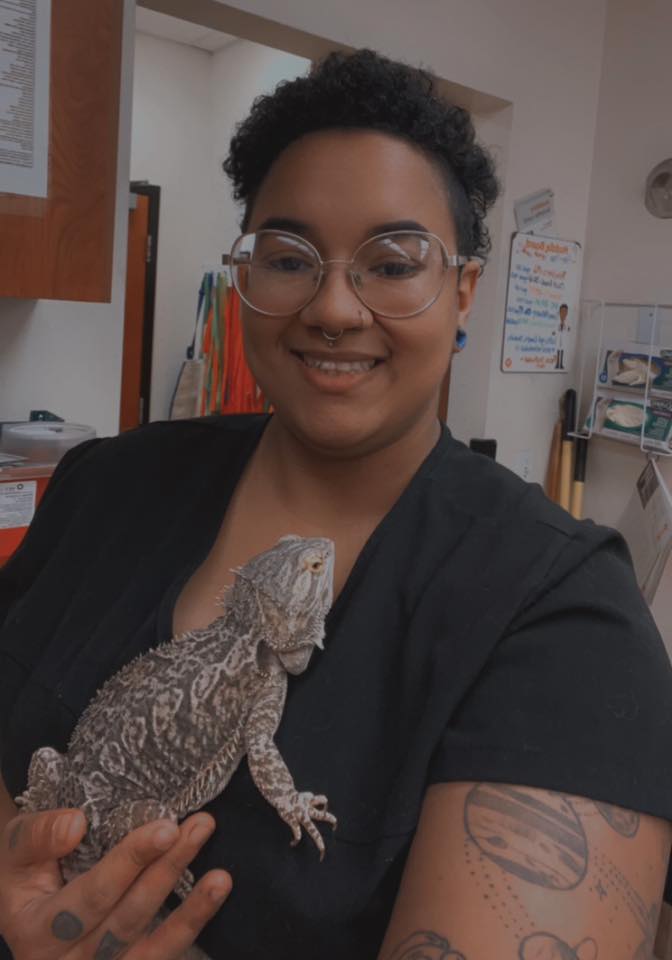 Jasmarie Dean smiling while holding a bearded dragon in an exam room