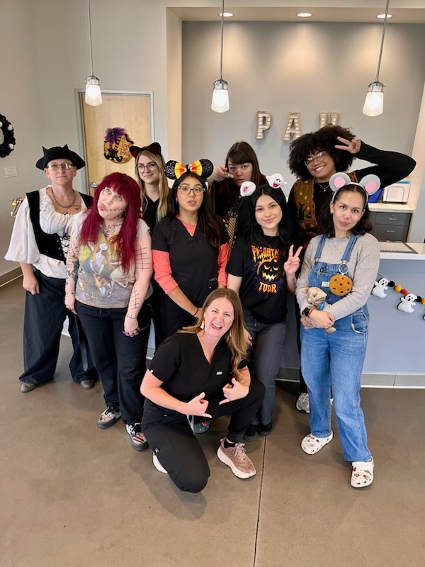 A veterinary hospital team in Halloween costumes posing together at the front desk